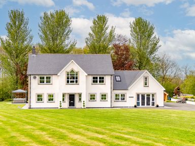 A large house with multiple windows and a gray roof surrounded by trees and lawns at Parc Y Deri in Rhos-y-garth near Aberystwyth