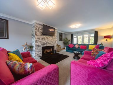 A living room with pink and teal sofas colorful pillows a fireplace and a wall-mounted TV at Parc Y Deri in Rhos-y-garth near Aberystwyth
