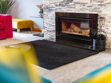 A living room with a stone fireplace a black hearth a pink chair a yellow ottoman and a glass side table at Parc Y Deri in Rhos-y-garth near Aberystwyth