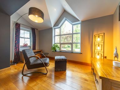 A room with a grey armchair a footstool a wooden cabinet and large windows at Parc Y Deri in Rhos-y-garth near Aberystwyth