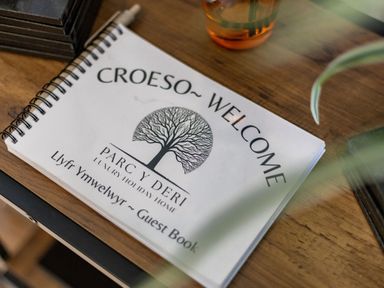 A guest book on a wooden table with a glass nearby at Parc Y Deri Rhos-y-garth near Aberystwyth