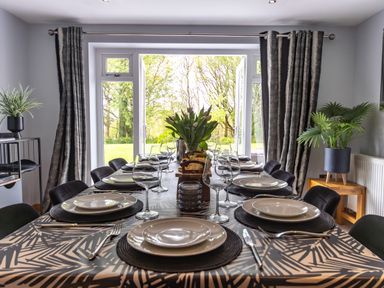 A dining room with a table set for a meal with plates glasses and cutlery and plants near large windows at Parc Y Deri Rhos-y-garth near Aberystwyth