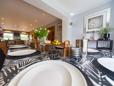 A dining table set with white plates wine glasses and black placemats with a vase of white tulips and fruit platter at Parc Y Deri in Rhos-y-garth near Aberystwyth