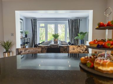 A dining area with a long table set for a meal and plants near large windows at Parc Y Deri in Rhos-y-garth near Aberystwyth