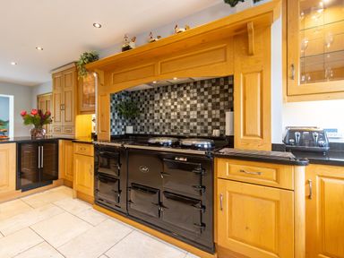 A kitchen with wooden cabinets black stove and patterned backsplash at Parc Y Deri in Rhos-y-garth near Aberystwyth
