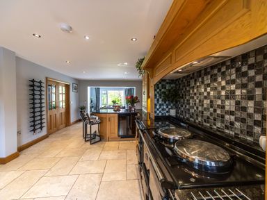 A kitchen with a large black stove a kitchen island with chairs and cabinets at Parc Y Deri in Rhos-y-garth near Aberystwyth