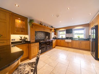 A kitchen with wooden cabinets a black countertop a large black stove two windows above the sink and a refrigerator at Parc Y Deri Rhos-y-garth near Aberystwyth