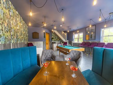 A game room with a pool table blue and purple chairs a brown table with drinks and hanging light bulbs at Parc Y Deri in Rhos-y-garth near Aberystwyth