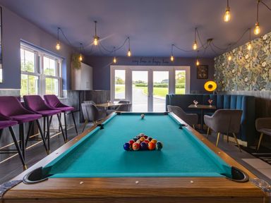 A room with a billiards table set up for a game surrounded by purple bar stools gray chairs and teal booth seating at Parc Y Deri in Rhos-y-garth near Aberystwyth