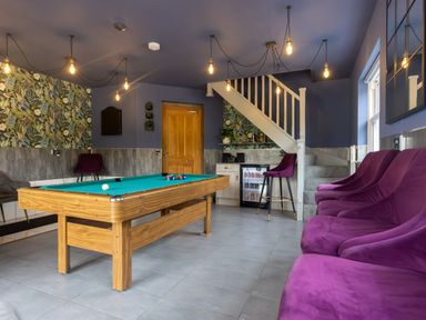 A room with a pool table purple chairs a small fridge under stairs and a wooden door at Parc Y Deri in Rhos-y-garth near Aberystwyth