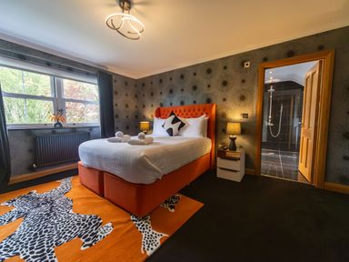 A bedroom with an orange bed and patterned rug next to a window and a nightstand with a lamp at Parc Y Deri in Rhos-y-garth near Aberystwyth