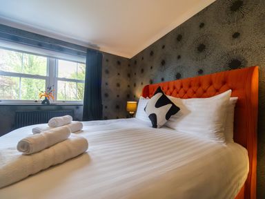 A bedroom with a bed with white linens and an orange headboard near a window with a black curtain and a small vase with flowers at Parc Y Deri Rhos-y-garth near Aberystwyth