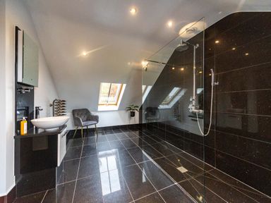 A bathroom with a glass shower, black tiled floor and walls, a sink, a chair, and a window at Parc Y Deri in Rhos-y-garth near Aberystwyth
