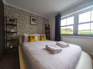 A bedroom with a double bed with white linens and yellow pillows near a window with black curtains at Parc Y Deri in Rhos-y-garth near Aberystwyth