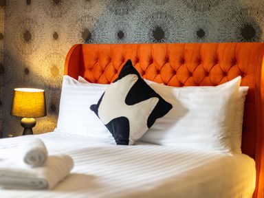 A bed with white sheets an orange tufted headboard a black and white pillow and a bedside lamp with patterned wallpaper at Parc Y Deri in Rhos-y-garth near Aberystwyth