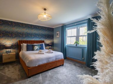 A bedroom with a bed with pillows and rolled towels bedside tables with lamps window with curtains and a plant at Parc Y Deri in Rhos-y-garth near Aberystwyth