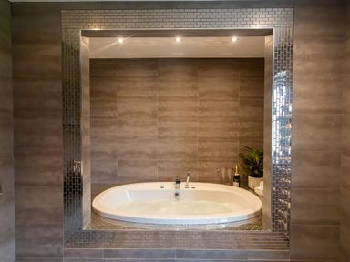 A bathroom with a built-in bathtub filled with water surrounded by brown tiles and a plant with bottles at Parc Y Deri in Rhos-y-garth near Aberystwyth