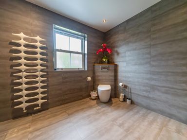 A bathroom with a toilet a window a white wall heater and a vase with red flowers at Parc Y Deri in Rhos-y-garth near Aberystwyth