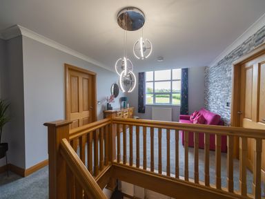 A landing area with wooden railing a pink sofa a wooden sideboard and a window at Parc Y Deri in Rhos-y-garth near Aberystwyth