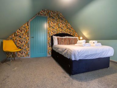 A bedroom with a double bed with folded towels on it a yellow chair and a blue door with patterned wallpaper at Parc Y Deri in Rhos-y-garth near Aberystwyth