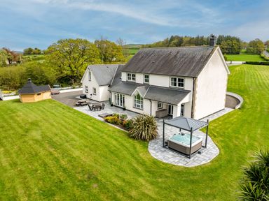 A house with a large lawn a hot tub a wooden gazebo and outdoor seating at Parc Y Deri in Rhos-y-garth near Aberystwyth
