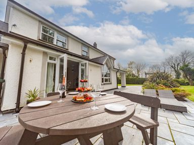A patio with a wooden round table set with plates glasses and pastries outside a white house at Parc Y Deri in Rhos-y-garth near Aberystwyth