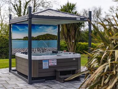 An outdoor hot tub under a gazebo with a backdrop showing a lake and trees at Parc Y Deri in Rhos-y-garth near Aberystwyth