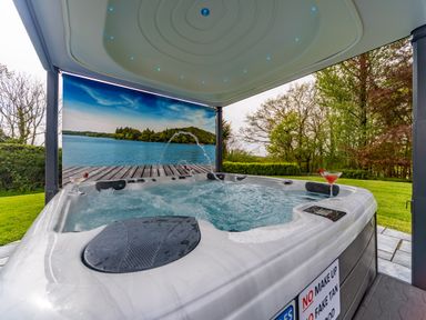 An outdoor hot tub with water jets and drinks under a covered structure with a scenic lake mural and surrounding trees at Parc Y Deri in Rhos-y-garth near Aberystwyth