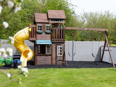 A wooden playhouse with yellow spiral slide and swings in a backyard at Parc Y Deri in Rhos-y-garth near Aberystwyth
