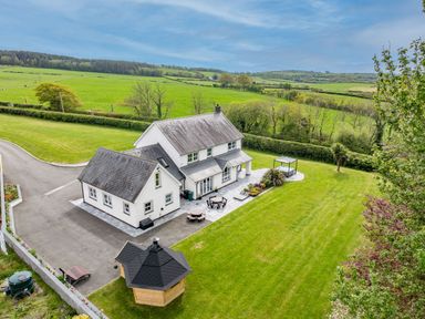 A detached white house with grey roofs surrounded by a lawn and garden furniture at Parc Y Deri in Rhos-y-garth near Aberystwyth