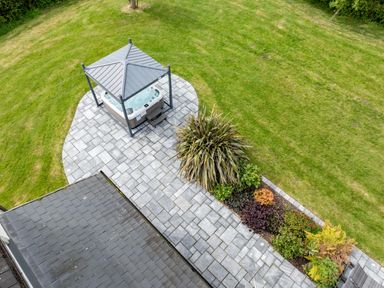 A hot tub with a canopy on a paved patio next to a garden bed and grass at Parc Y Deri in Rhos-y-garth near Aberystwyth