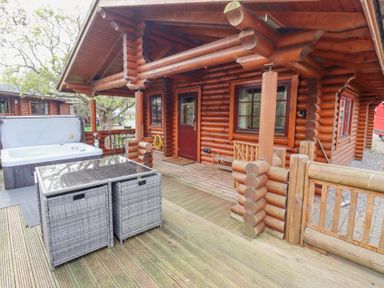 A wooden log cabin exterior with a hot tub and outdoor furniture on a wooden deck at 24 Lakeside Drive in Felton