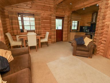 A living area with a brown sofa and armchair next to a wooden dining table with four white chairs and a small kitchen with wooden cabinets at 24 Lakeside Drive in Felton