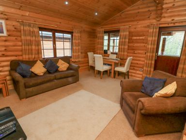 A living room with two brown sofas with cushions a small dining table with four chairs and wooden walls and ceiling at 24 Lakeside Drive in Felton