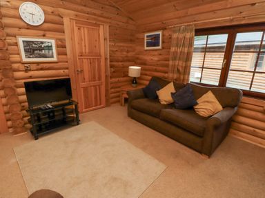 A living room with a brown sofa and cushions a lamp on a side table a television on a stand a wall clock and framed pictures at 24 Lakeside Drive in Felton