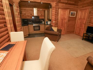 A living area with a dining table and chairs a kitchen with wooden cabinets a brown armchair and a television on a stand at 24 Lakeside Drive in Felton