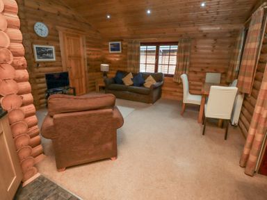 A living room with wooden walls a sofa armchair small dining table and TV at 24 Lakeside Drive in Felton