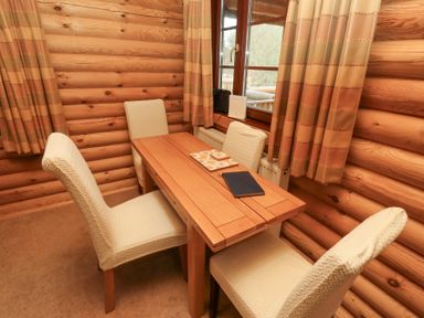 A wooden dining table with four cream chairs near a window with beige curtains at 24 Lakeside Drive in Felton