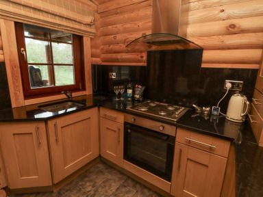 A kitchen with wooden cabinets black countertops a gas stove an oven a sink a window and small appliances at 24 Lakeside Drive in Felton