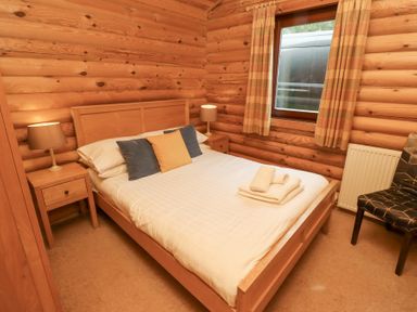 A bedroom with a wooden bed frame white bedding pillows two bedside tables with lamps a window with curtains and a chair at 24 Lakeside Drive in Felton