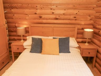 A bed with three pillows and two bedside tables with lamps in a wooden room at 24 Lakeside Drive in Felton