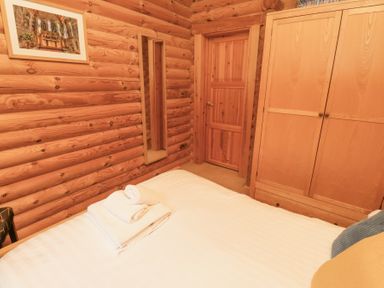 A bedroom with a bed and folded towels on it a wooden wardrobe a door a wall mirror and a framed picture on wooden log walls at 24 Lakeside Drive Felton