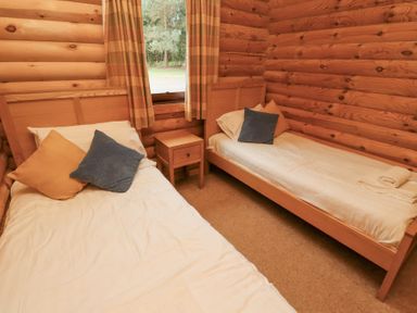 A bedroom with two single beds one bedside table between them and a window with curtains at 24 Lakeside Drive Felton