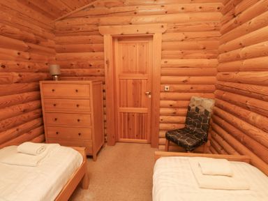 A bedroom with two single beds towels on beds a wooden chest of drawers with lamp and a patterned chair at 24 Lakeside Drive in Felton