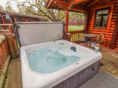 An outdoor hot tub with bubbling water on a wooden deck next to a table with chairs and wine glasses at 24 Lakeside Drive in Felton
