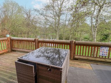 A wooden deck with a glass-top table and woven chairs overlooking trees and a pond at 24 Lakeside Drive in Felton