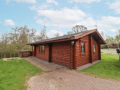 A wooden log cabin with windows and a small patio surrounded by grass and trees at 24 Lakeside Drive in Felton