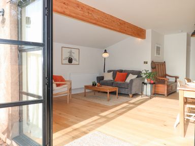 A living room with a grey sofa and a wooden chair near a coffee table and wooden dining table at Church Farm Dairy in Cadbury near Thorverton