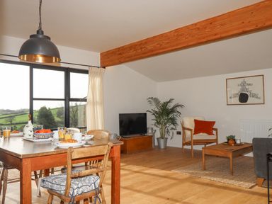 A dining area with a wooden table set for breakfast and a living room with a chair TV and coffee table at Church Farm Dairy Cadbury near Thorverton