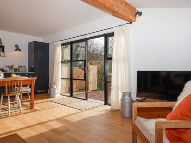A living room with wooden dining table and chairs and glass doors leading outside at Church Farm Dairy in Cadbury near Thorverton